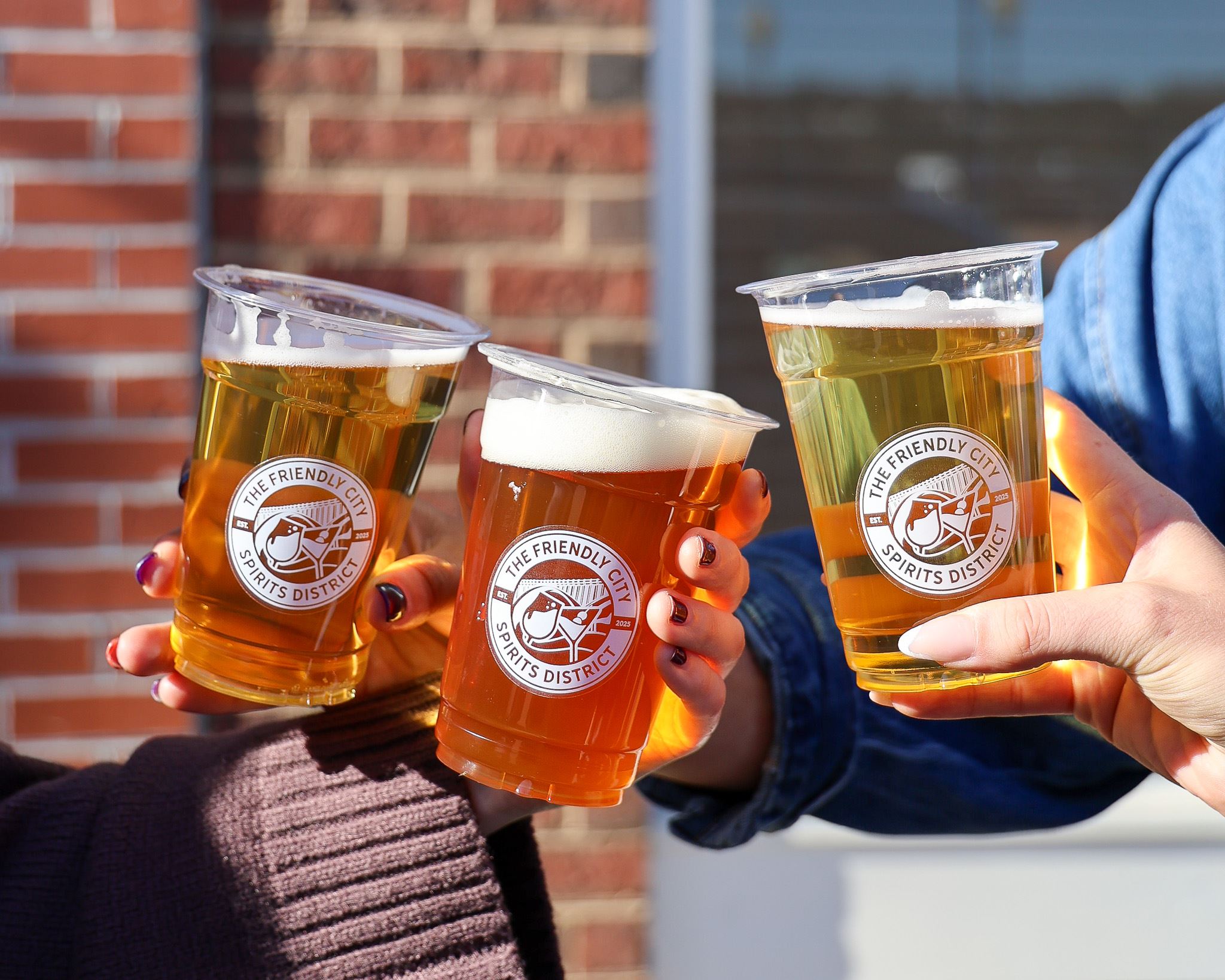 Three PODA cups toasting in front of a brick wall.